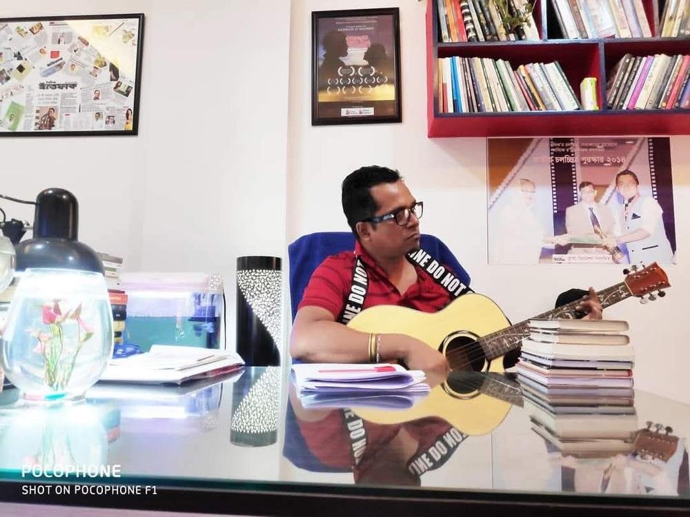 Masud Pathik at his desk with a guitar