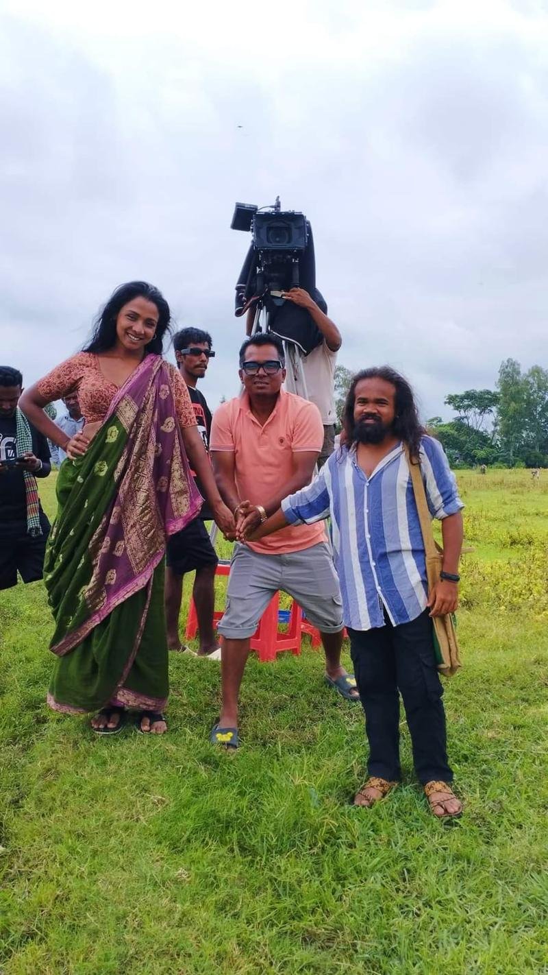 Masud Pathik on location in a green field with cast members and a camera crew behind